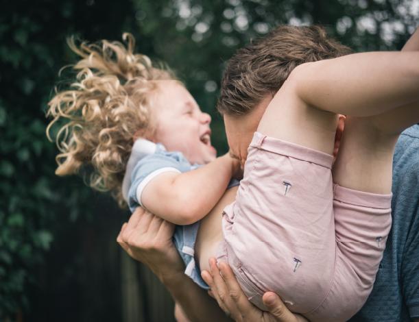 pikkulapsi nauraa isän sylissä